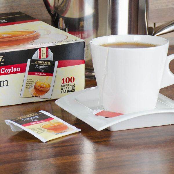 A package of Bigelow Premium Ceylon Tea on a table next to a cup of tea on a saucer.
