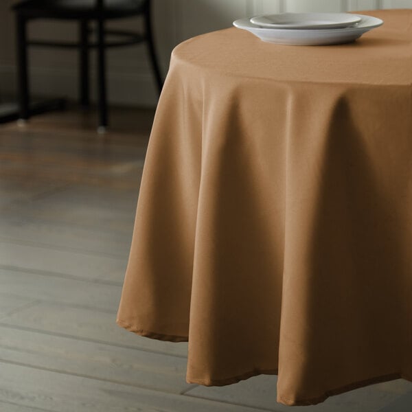 A table with a brown Intedge 100% polyester round tablecloth and a plate on it.