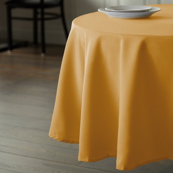 An Intedge gold polyester table cover on a round table with a white plate.