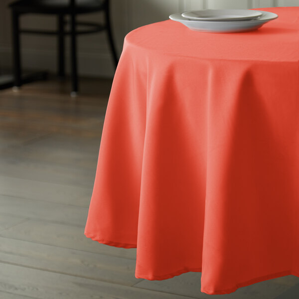 An orange Intedge round polyester table cover on a table