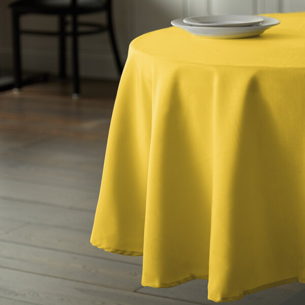 A table with an Intedge yellow tablecloth on it with a white plate.