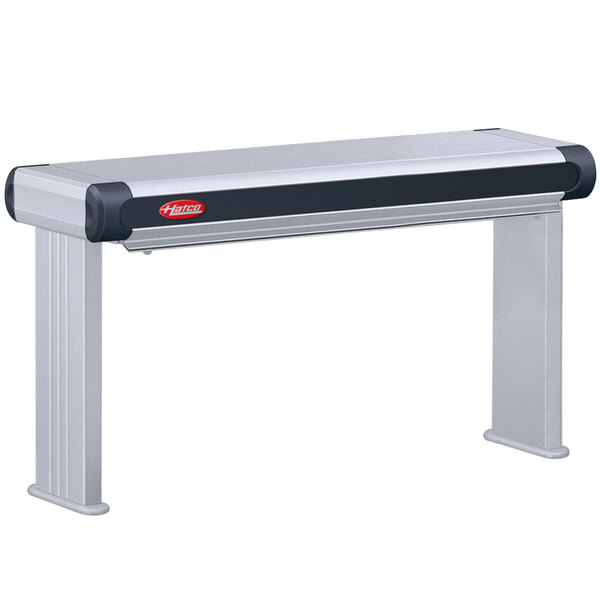 A grey and black rectangular Hatco strip warmer on a table with a metal shelf and remote controls.