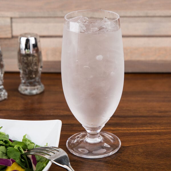 A close-up of a customizable Tritan plastic goblet filled with water on a table next to a salad plate.