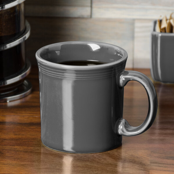A Slate Fiesta Java mug with a handle filled with coffee on a wooden table.