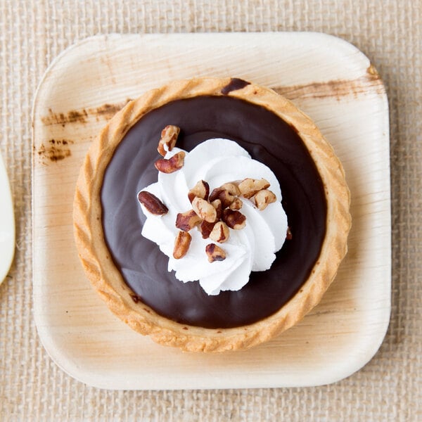 A chocolate tart with whipped cream and nuts on an Eco-gecko palm leaf plate.