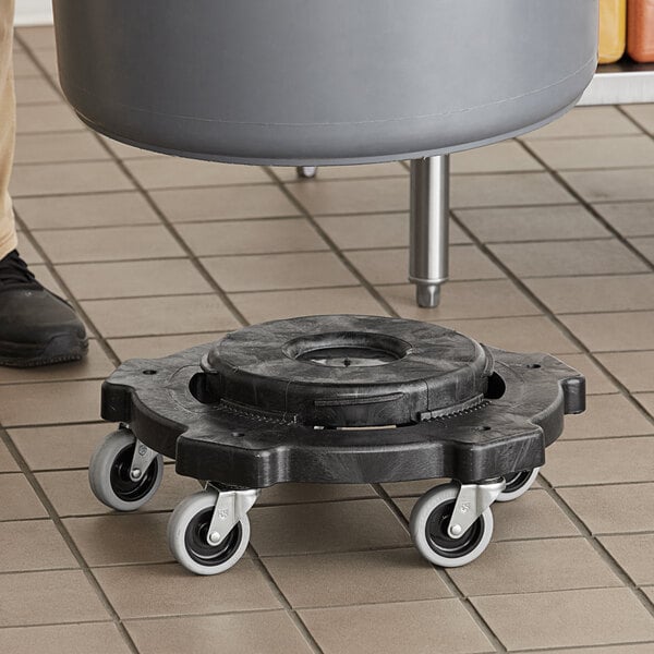A black Lavex Commercial round trash can dolly with wheels on a tile floor.