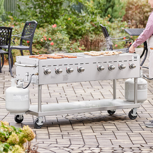 A man cooking food on a Backyard Pro stainless steel outdoor grill on a table in an outdoor setup.