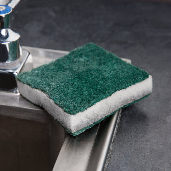 A green Scrubble tough-scour nylon soap pad on a metal surface.