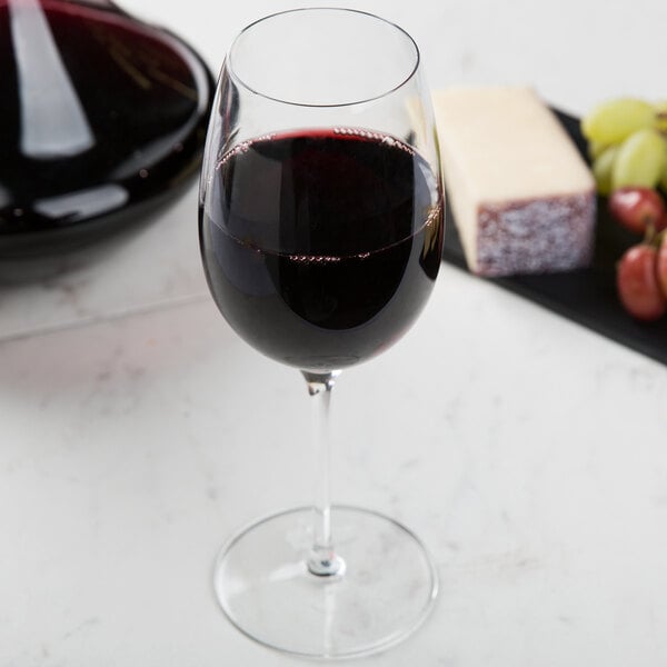 A close-up of a Reserve by Libbey wine glass filled with red wine on a table with a piece of cheese.