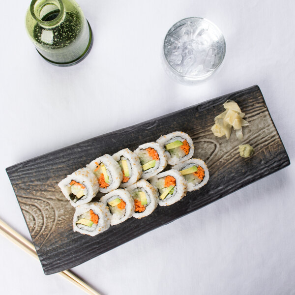 A rectangular stoneware slab with sushi rolls and chopsticks on a table.