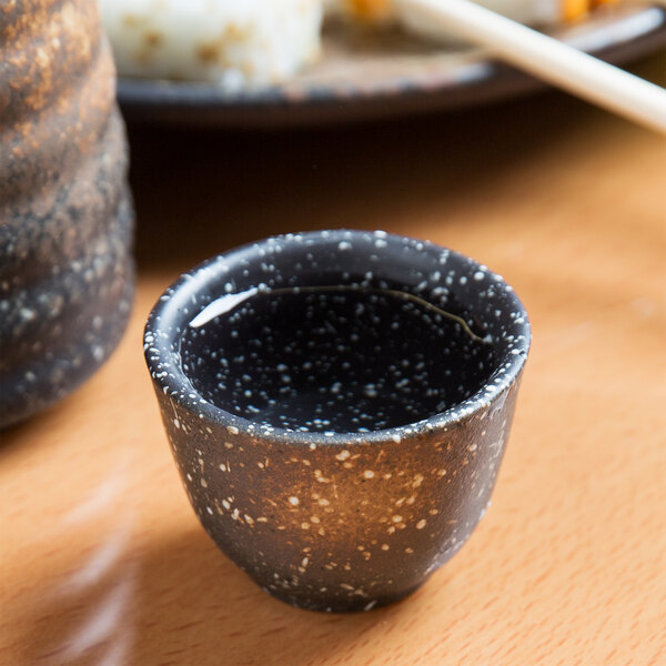 A black stoneware sake cup with white specks on a wooden surface.