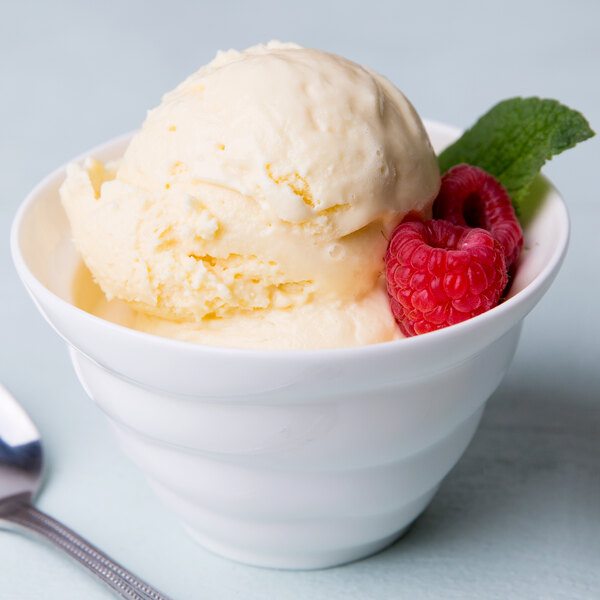 A 10 Strawberry Street bright white porcelain sorbet cup filled with ice cream, raspberries, and mint with a spoon.