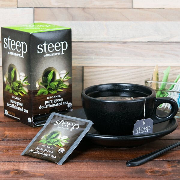 A cup of Steep by Bigelow decaffeinated green tea next to a box of Steep by Bigelow organic decaffeinated green tea.