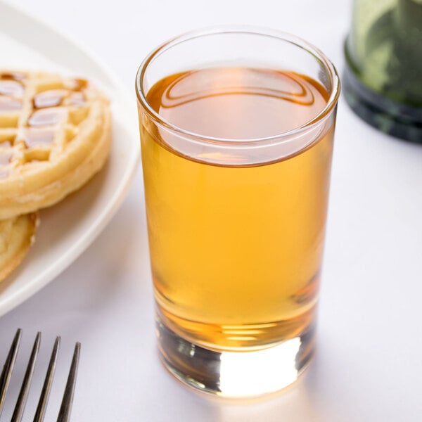 An Arcoroc Islande juice glass filled with brown liquid next to a plate of waffles.