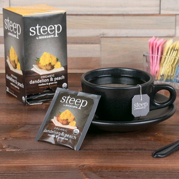 A black cup and saucer with a packet of Steep By Bigelow Organic Dandelion and Peach Tea on a wooden table.