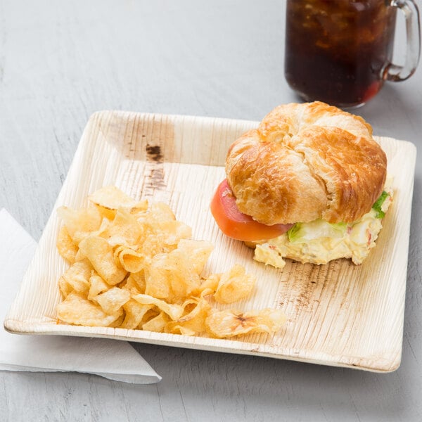 A croissant sandwich and chips on an EcoChoice palm leaf plate.