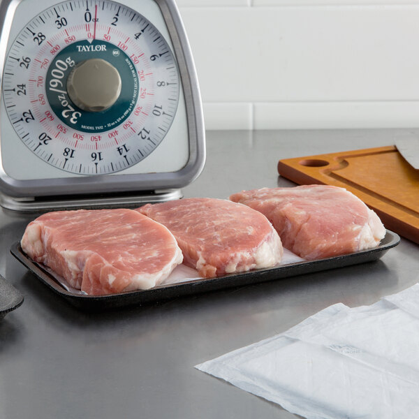 A black CKF foam meat tray holding a piece of raw meat on a counter.