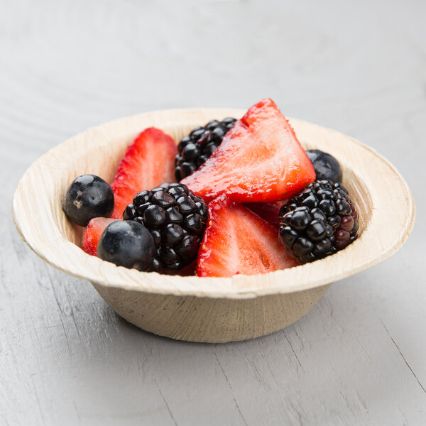 A EcoChoice palm leaf bowl filled with strawberries and blackberries on a table.