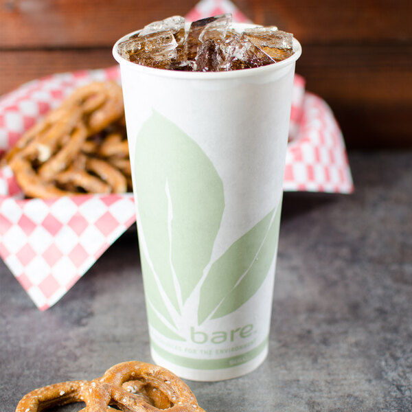 A white Bare by Solo paper cold cup with a green leaf design filled with ice tea and pretzels.