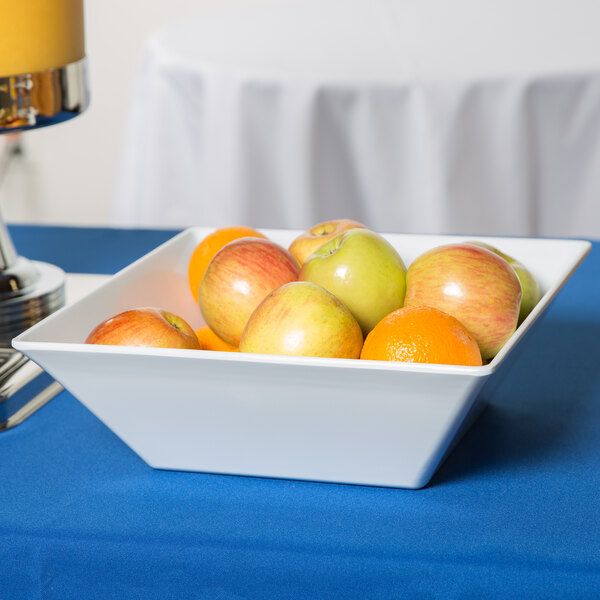 A white Siciliano square bowl filled with apples and oranges on a table.