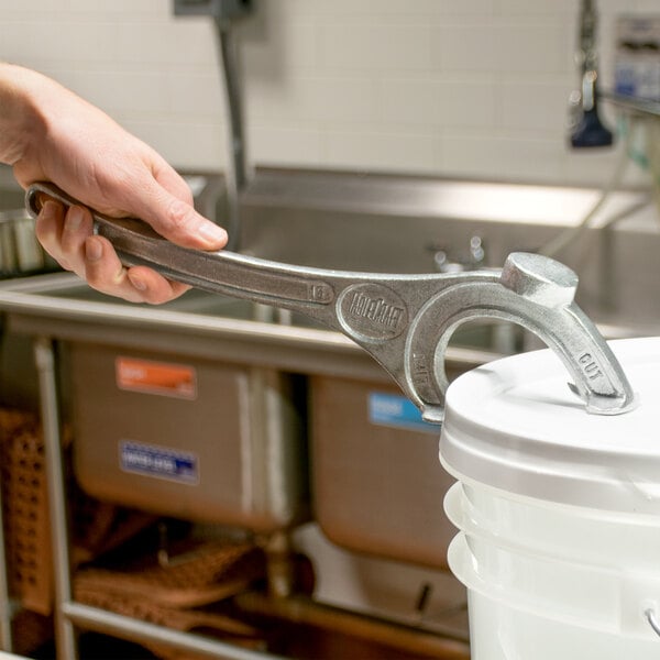 A hand using a Tablecraft Pail Opener to open a white bucket.