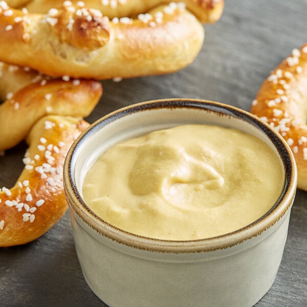 A bowl of Grey Poupon Dijon Mustard with pretzels on a table.