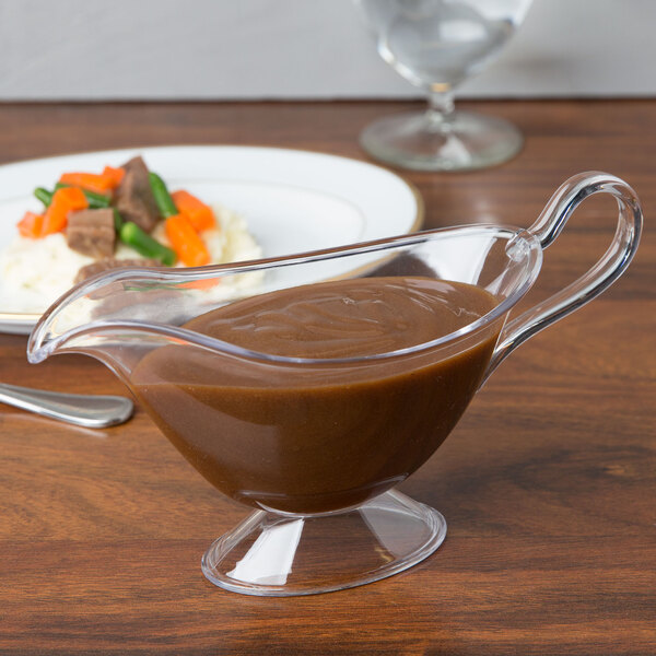 A Fineline clear plastic gravy boat on a table with food.