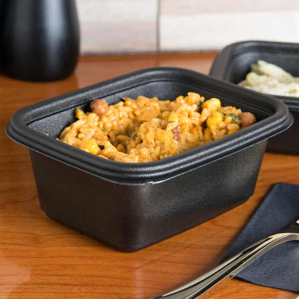 Two black Genpak Smart-Set Pro rectangular containers with food inside on a table.