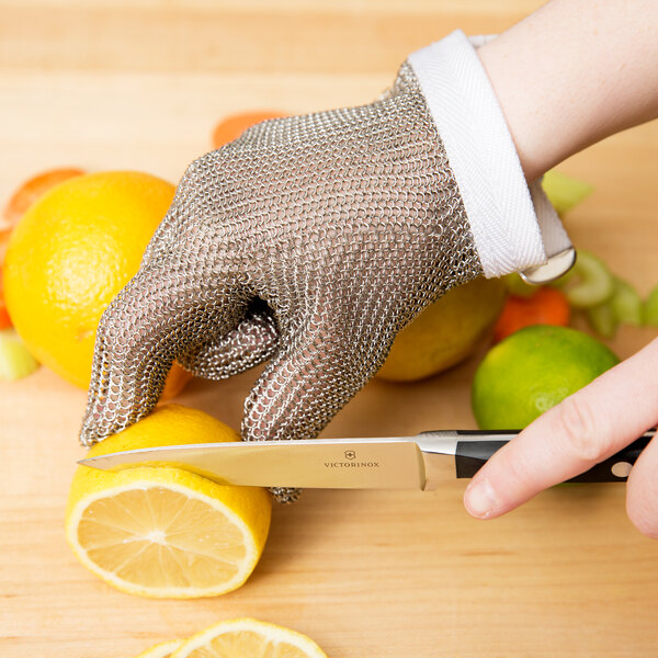 A person wearing a San Jamar stainless steel mesh glove cuts a lemon.