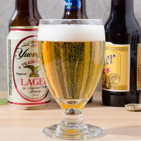 A Libbey Banquet Goblet filled with beer sits on a table with bottles of beer.
