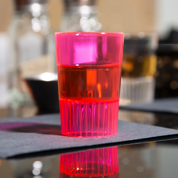 A close up of a Fineline neon red plastic shooter glass with red liquid in it.
