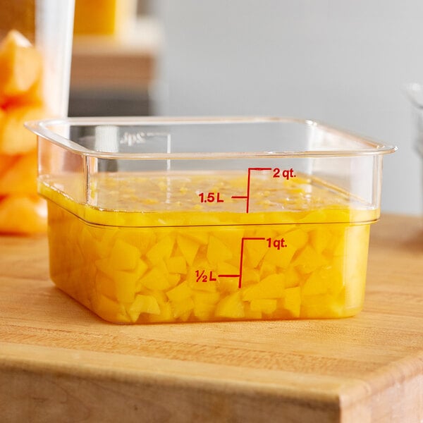 A Cambro CamSquares clear food storage container on a counter with yellow food inside.