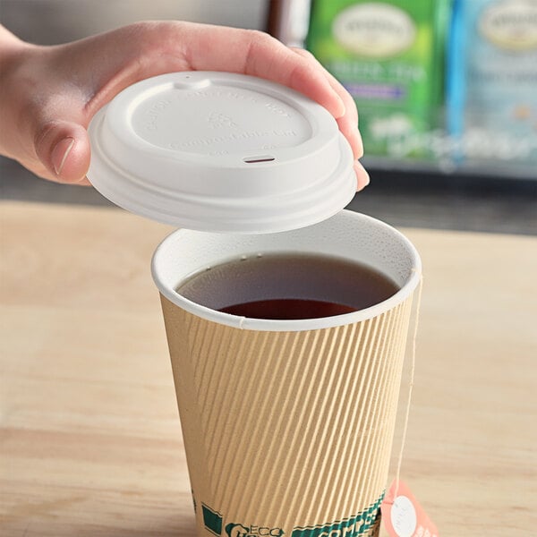 A hand using a white EcoChoice paper hot cup lid to top a cup of tea.