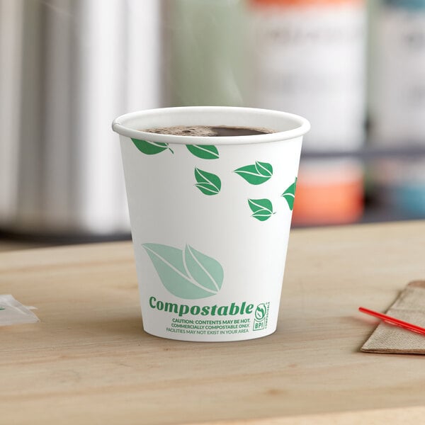 A EcoChoice paper hot cup with a green leaf print filled with coffee on a table.