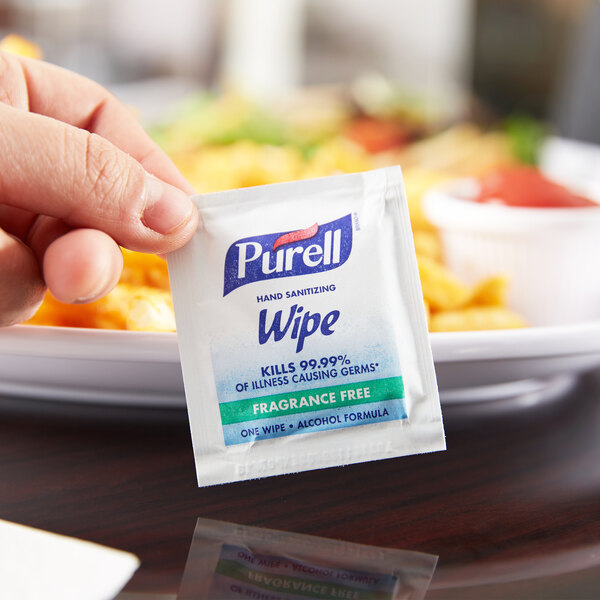 A hand holding a small packet of Purell hand sanitizing wipes.