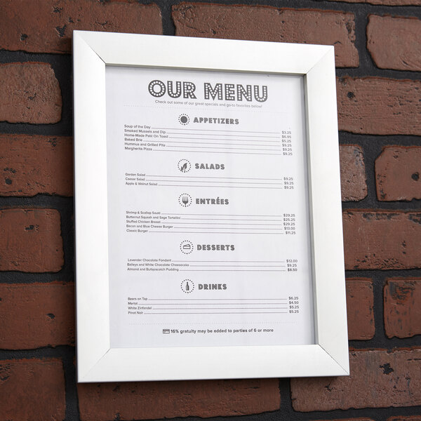 A white Aarco snap frame holding a menu on a brick wall.