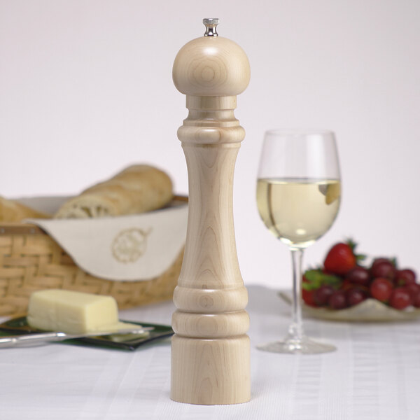 A wooden pepper mill on a table next to a glass of wine.