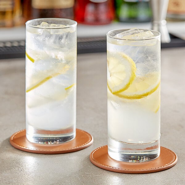 Two Acopa Collins glasses of water with lemon slices on coasters.