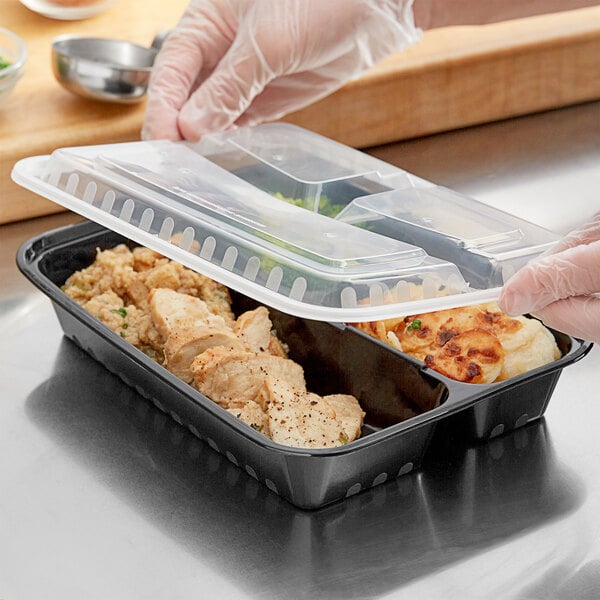 A gloved hand holds a Choice black rectangular plastic container with 3 compartments filled with food.