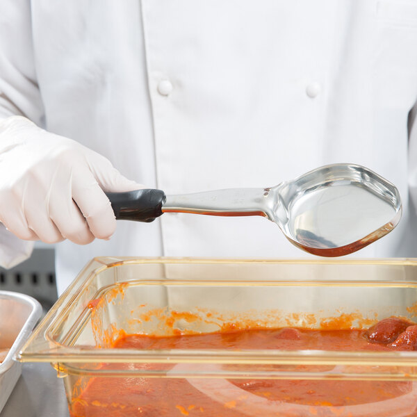 A person in white gloves using a Vollrath black solid oval Spoodle to serve food.