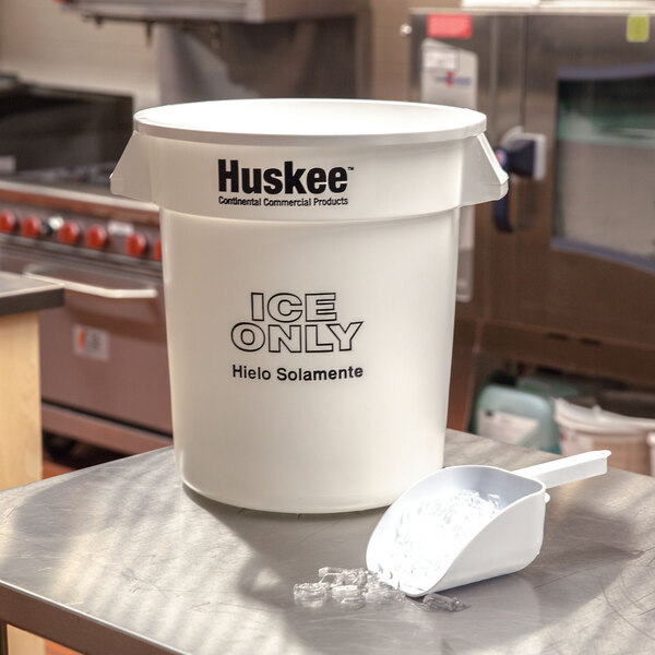 A white Continental Huskee ice bucket on a table with a white plastic scoop inside.