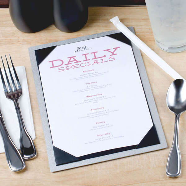 A Menu Solutions brushed aluminum menu board on a table with a fork and a glass of water.