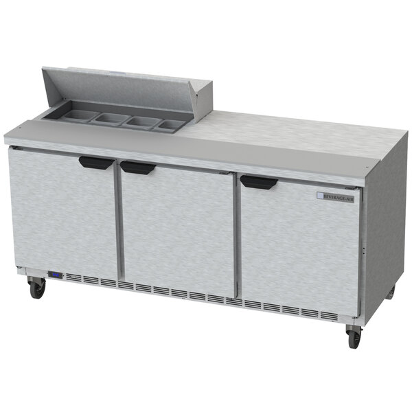 A Beverage-Air stainless steel refrigerated sandwich prep table with three doors and a cutting board.