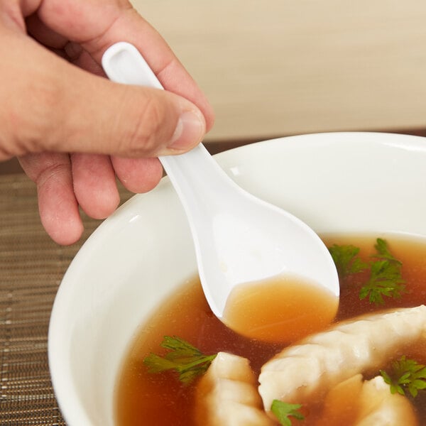A person holding a white melamine soup spoon over a bowl of brown soup.