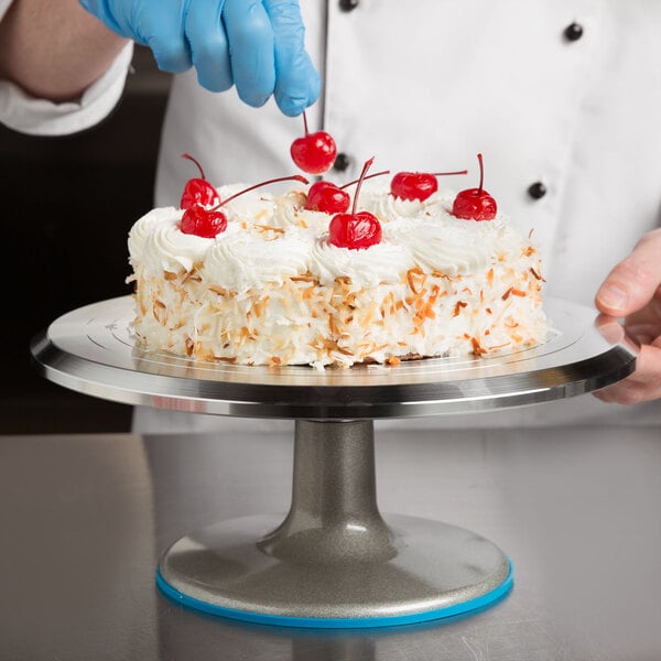 A person using an Ateco revolving cake stand to put cherries on a cake.