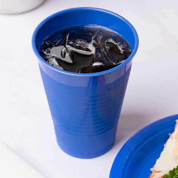 A cobalt blue plastic cup with ice in it next to a sandwich.