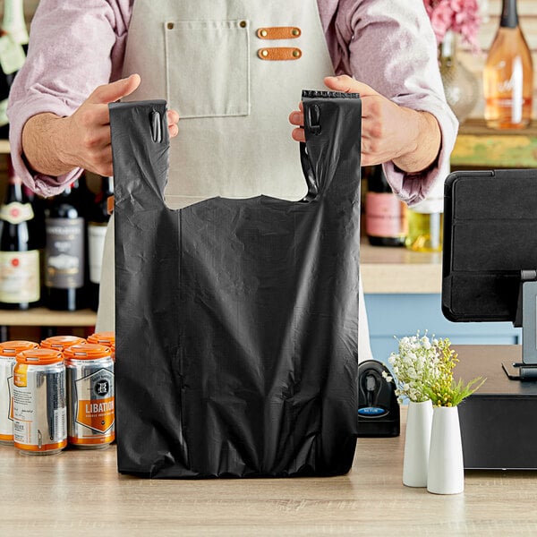 A person holding a black Choice heavy-duty plastic T-shirt bag on a counter.