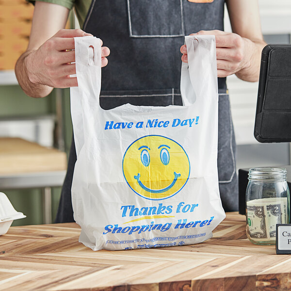 A person holding a white plastic t-shirt bag with a happy face on it.