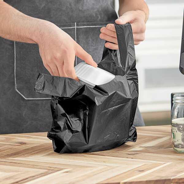 A person's hand putting a black plastic bag into a white plastic bag.