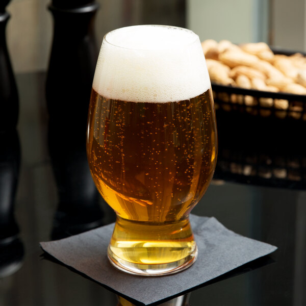 A Spiegelau American wheat beer glass full of beer with foam on a table.